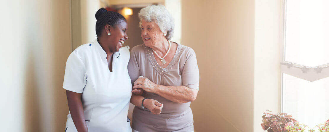 Happy female caregiver and senior woman walking together